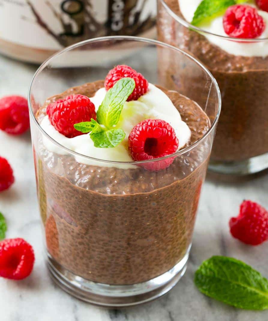 Chocolate Chia Protein Pudding in a glass cup topped with a small portion of yogurt, 3 fresh raspberries, and a small mint leaf.