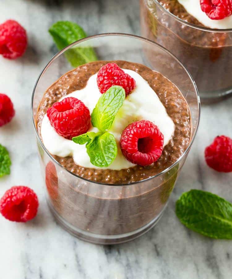 Chocolate Chia Protein Pudding in a glass cup topped with a small portion of yogurt, 3 fresh raspberries, and a small mint leaf.