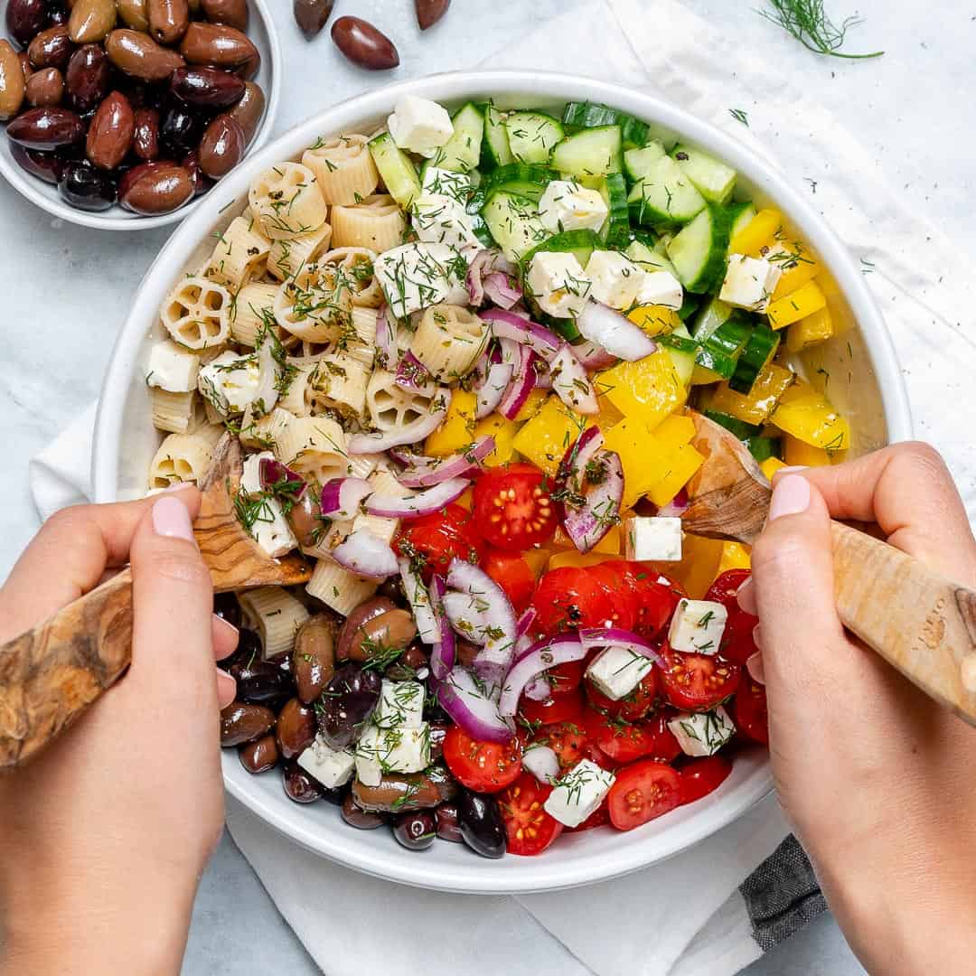 pasta, cucumber, tomatoes, olives, onions, feta cheese, peppers and herbs. in a bowl