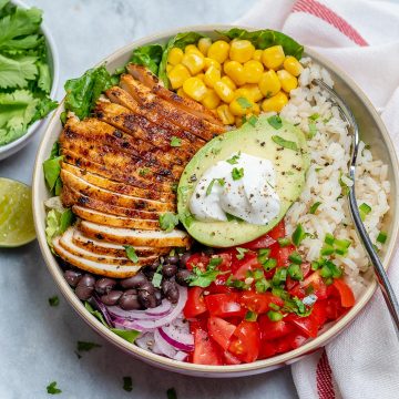 top view of a burrito bowl with sliced grilled chicken, rice, black beans, corn, tomatoes, and half avocado in the middle