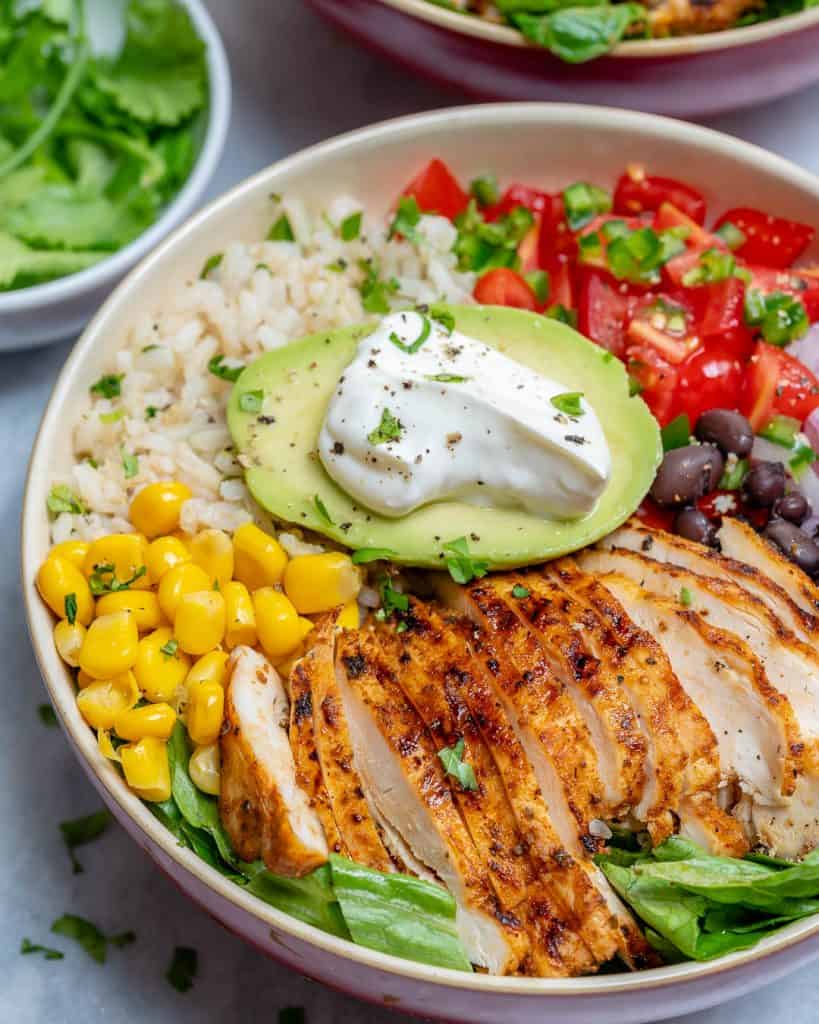 side shot of a burrito bowl with Grilled Chicken  corn, rice, tomatoes, beans, and avocados