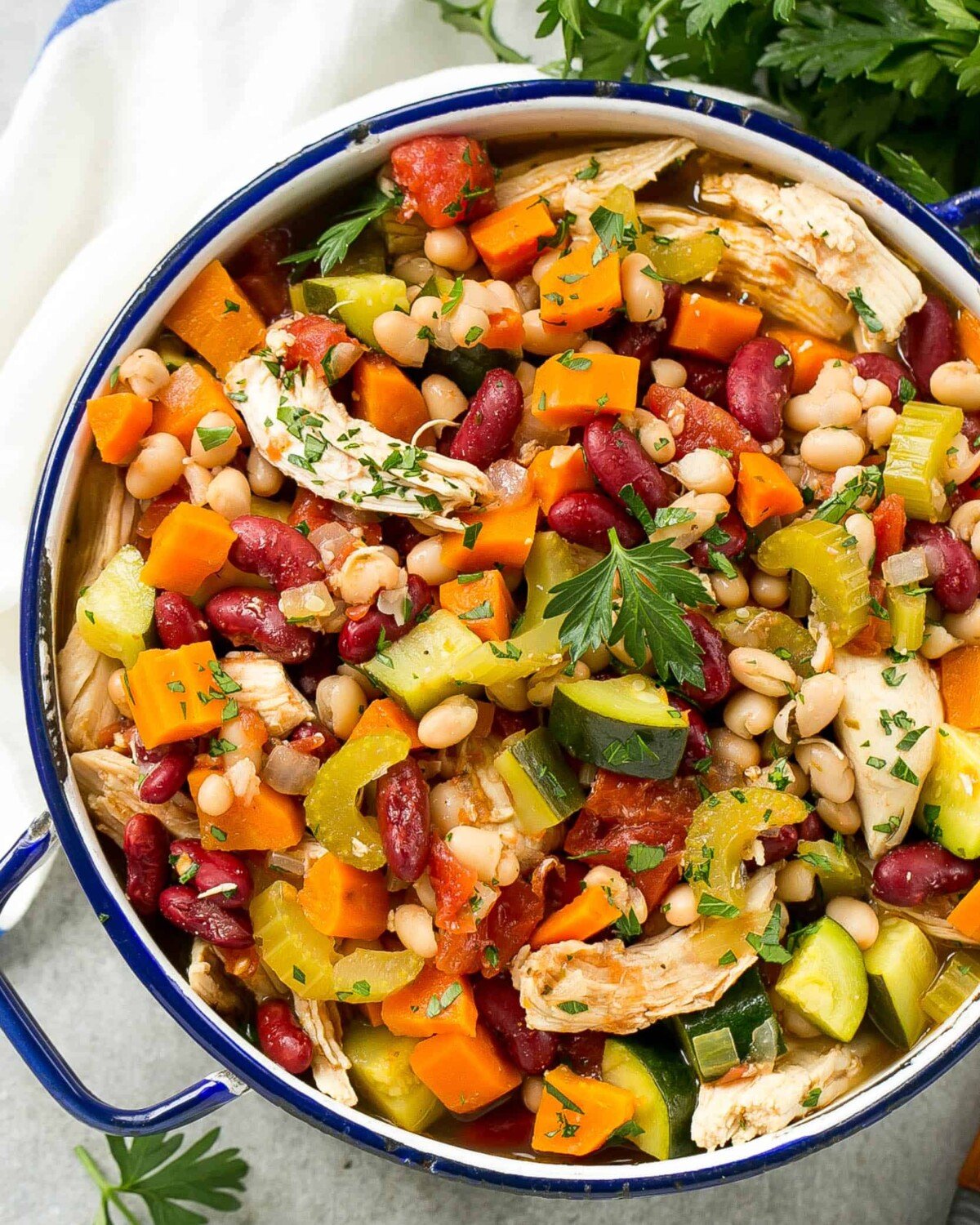 a round blue pot with chicken beans and veggies soup.