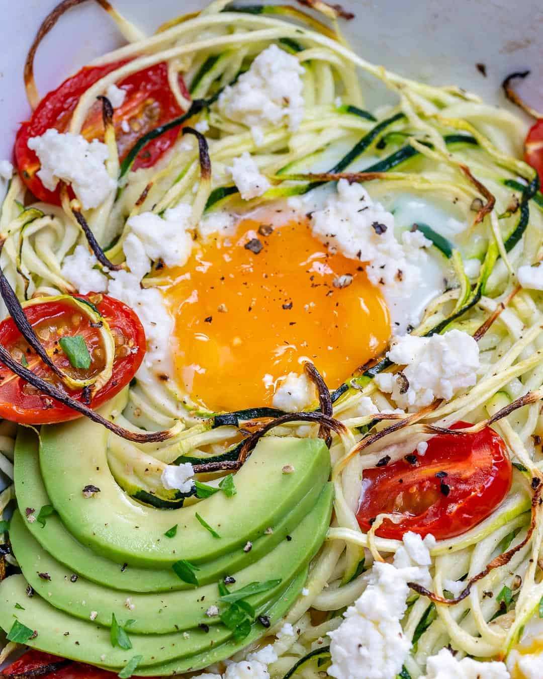 baked egg in a dish with zoodles and sliced avocado.