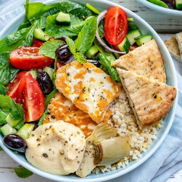 a round Mezze bowl with greens, grilled halloumi, hummus, and pita.