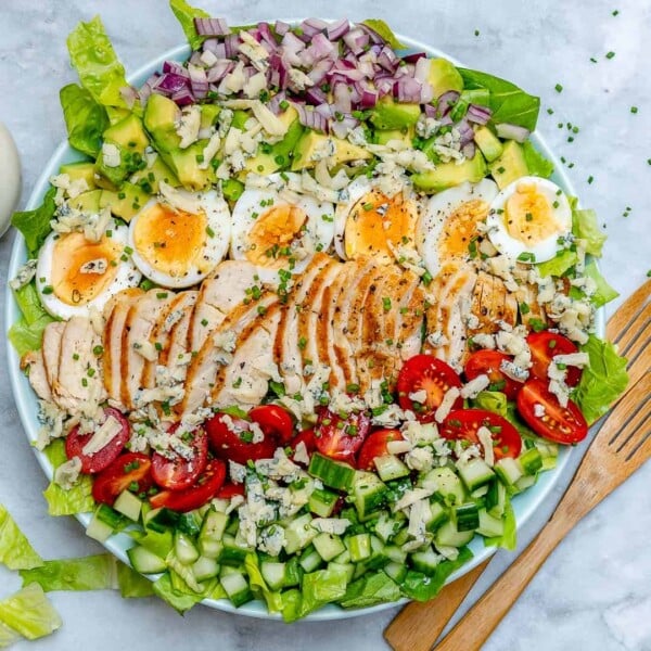 top view of a round bowl with chicken cobb salad and wooden serving spoon next to it