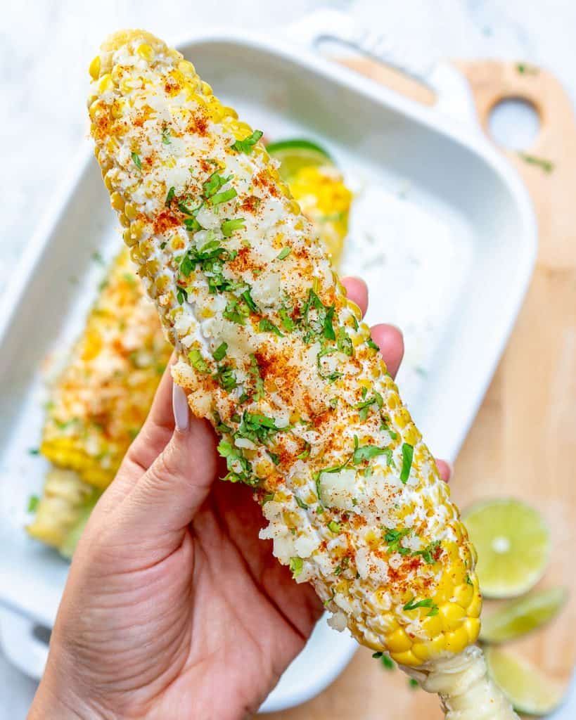 hand holding a single corn on the cob topped with crumbled cheese
