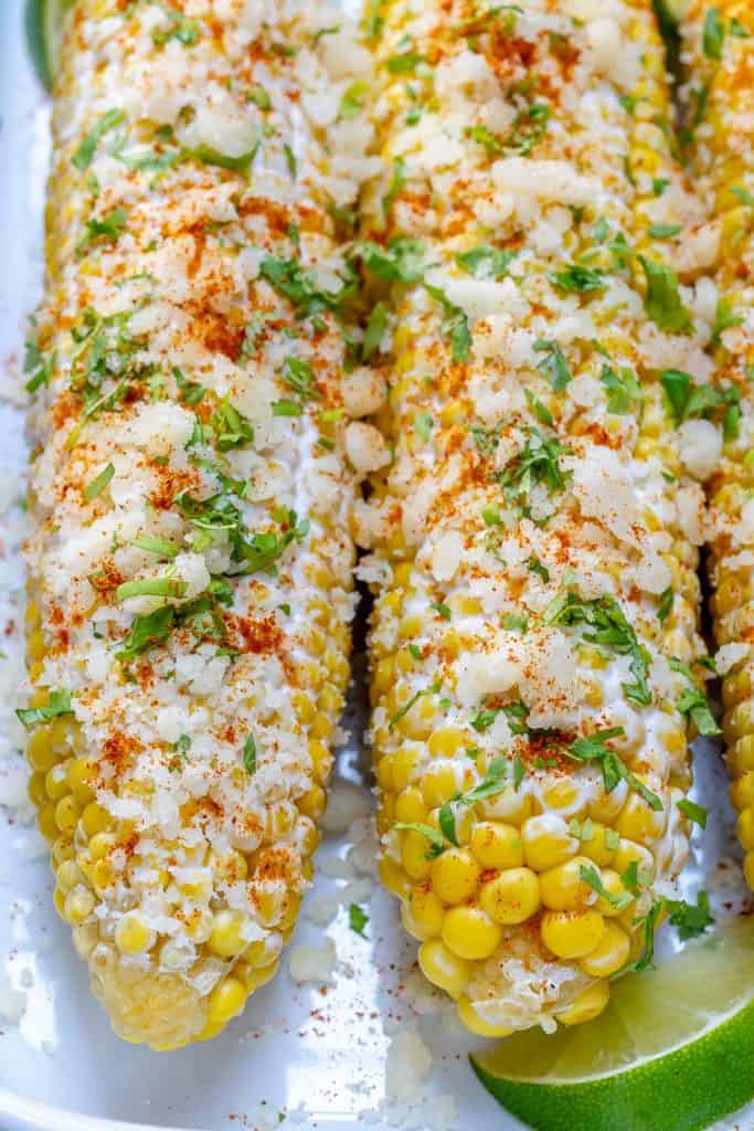 close up corn on the cob topped with crumbled cotija cheese and chopped cilantro