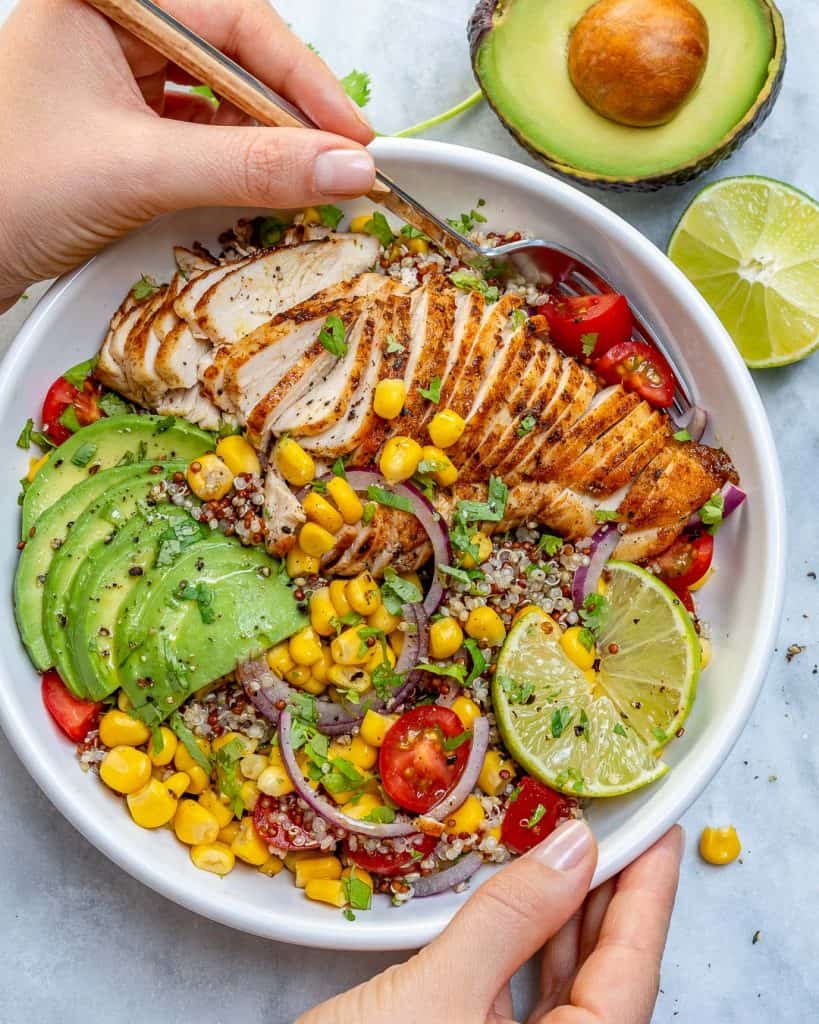 hand holding a bowl of Mexican grilled chicken  with quinoa avocado corn and tomatoes