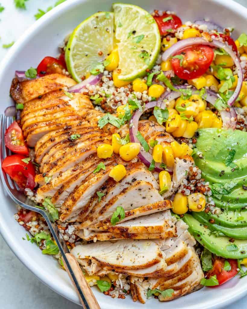 side shot of mexican grilled chicken in a bowl with quinoa avocado corn and chopped tomatoes with lime garnish