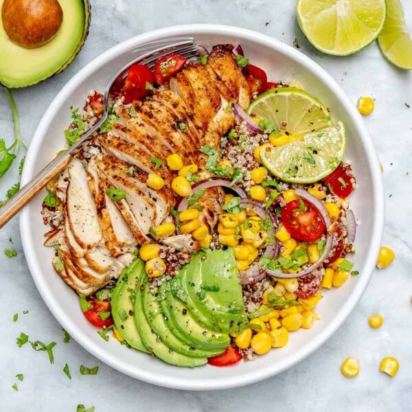 top view of grilled Mexican chicken bowl recipe with quinoa corn avocado, tomatoes with spoon on the left side of the bowl