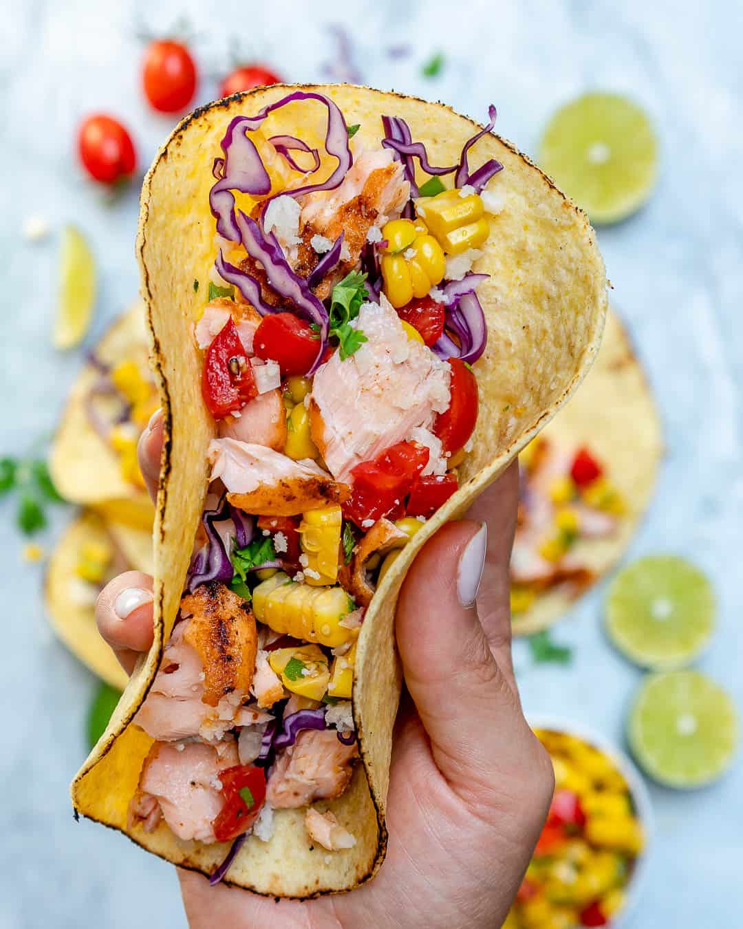 holding salmon fish tacos that's topped with corn salsa