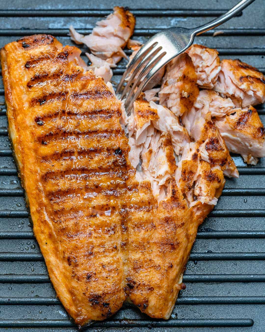 grilled salmon fillet on a griddle and shredding with fork