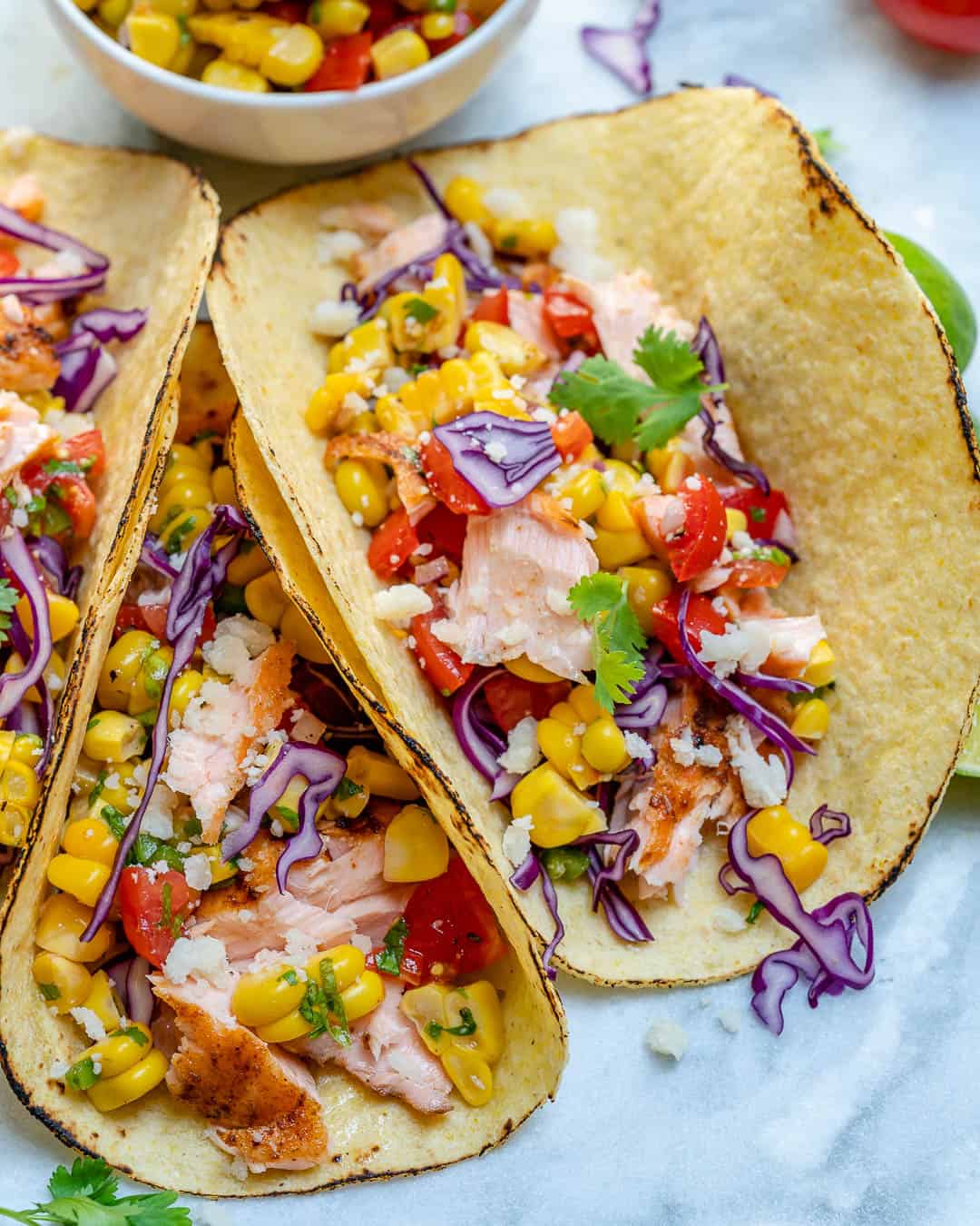 three tacos laid flat together with corn salsa bowl on the side