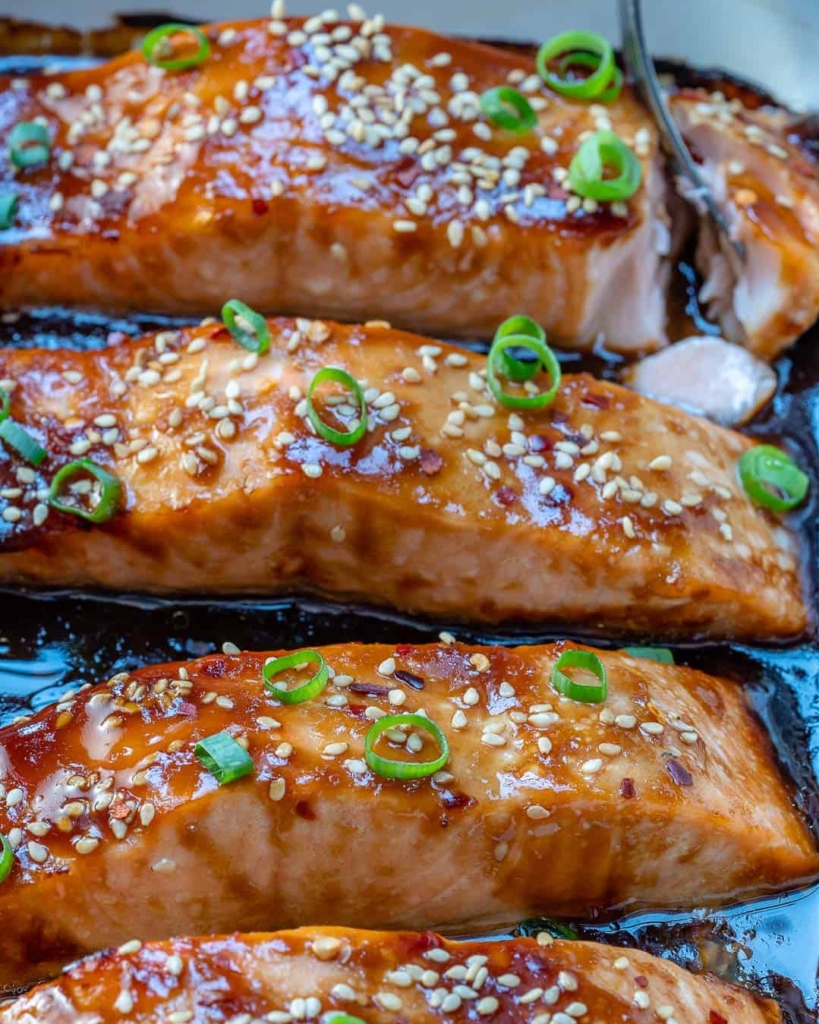 side view of 3 salmon baked in a white dish with sesame seed garnishes 