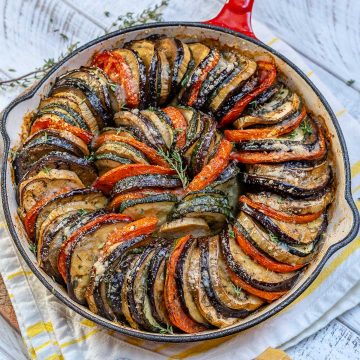 top view of a skillet with baked slices of eggplant, zucchini, and tomatoes stacked next to each other and topped with shredded parmesan chesse
