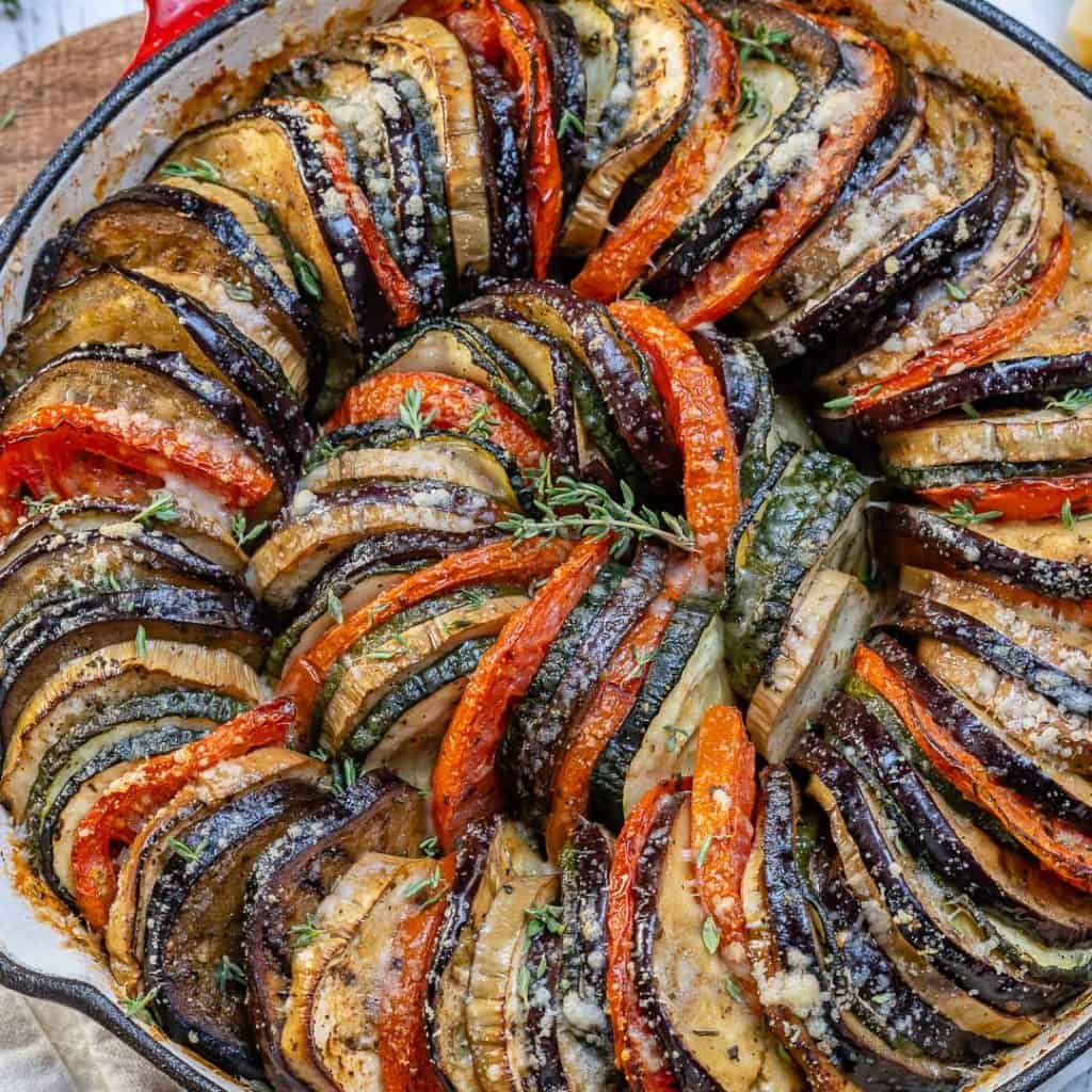 stacked slices of eggplant zucchini and tomatoes, in a skillet topped with parmesan cheese