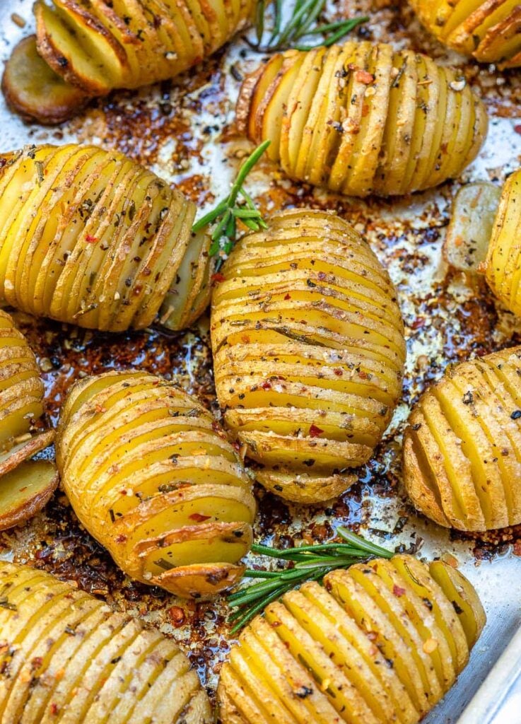 baked sliced potatoes on a sheet pan with fresh rosemary