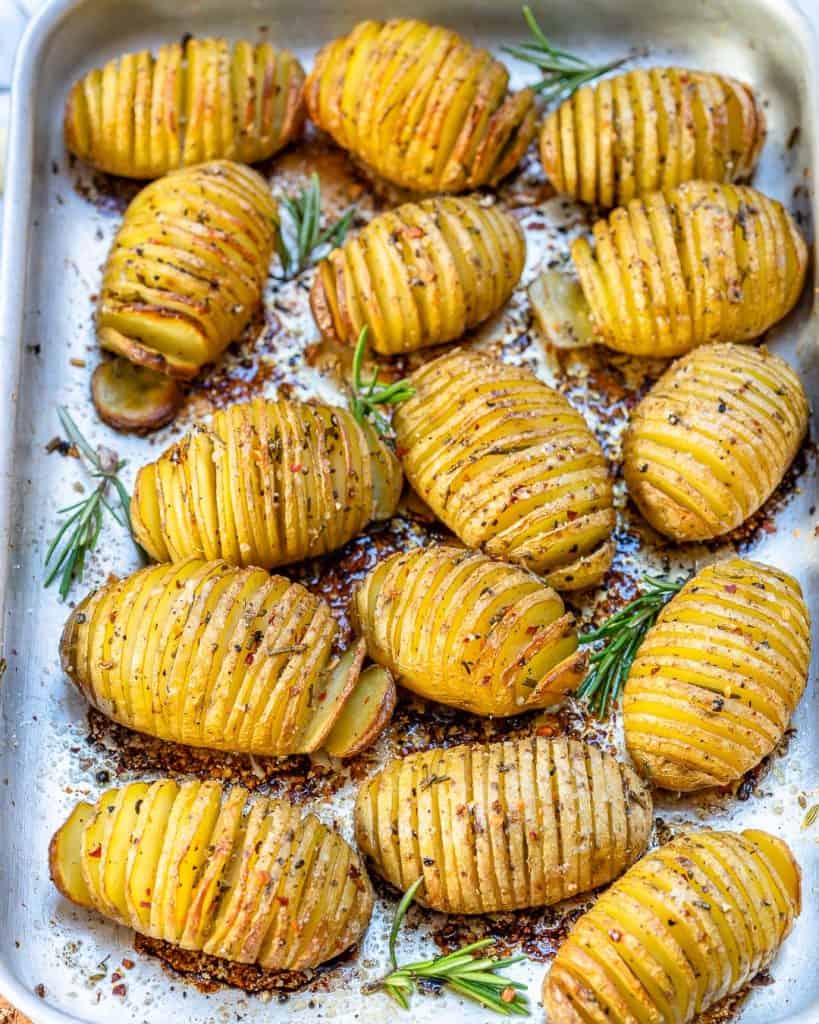 top view of baked sliced potatoes on a sheet pan with rosemary garnish