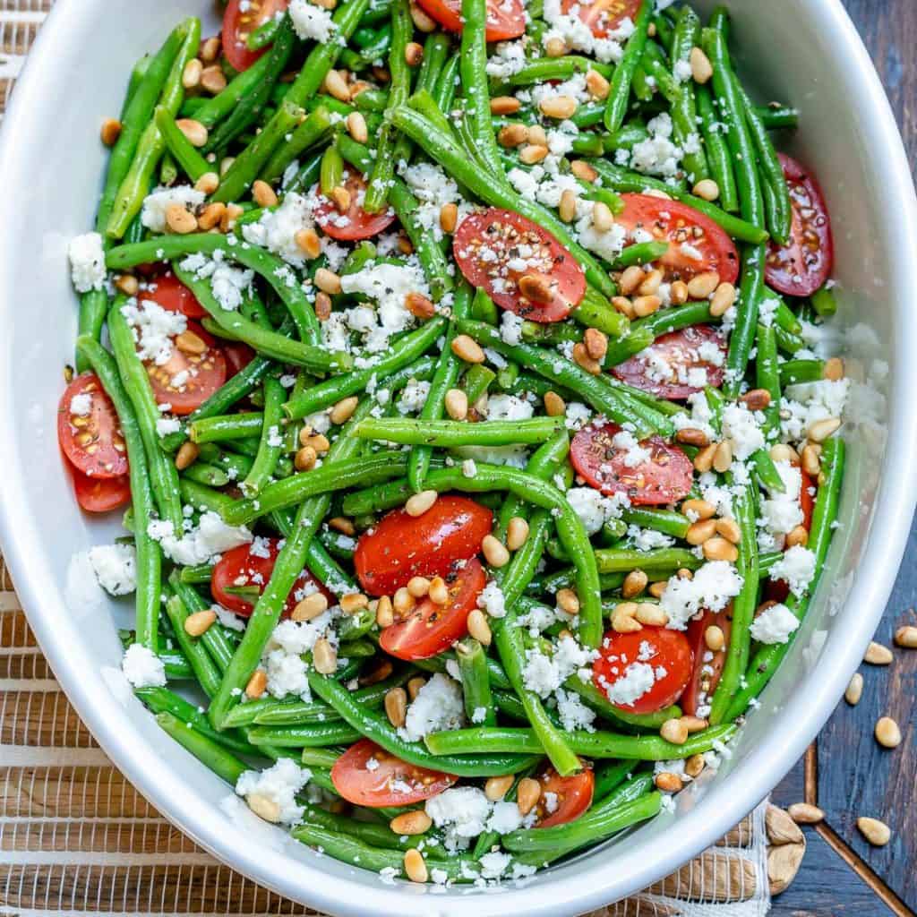 top view of green bean salad in a white bowl with feta cheese and cherry tomatoes 