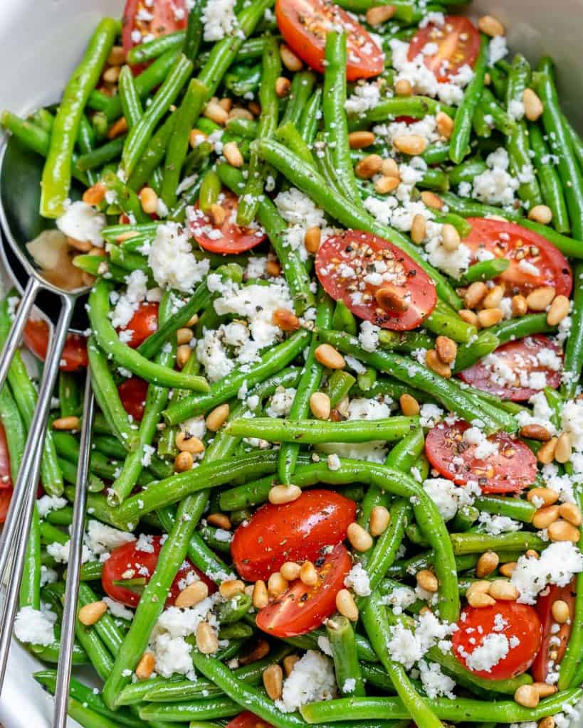 close up top view of green bean salad in a white bowl with feta cheese and cherry tomatoes 