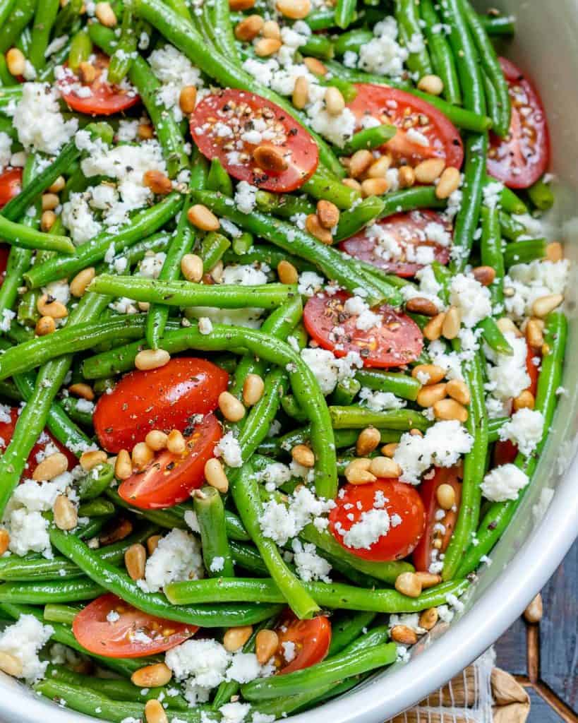 close up image of green bean salad in a white bowl topped with pine nuts and feta cheese