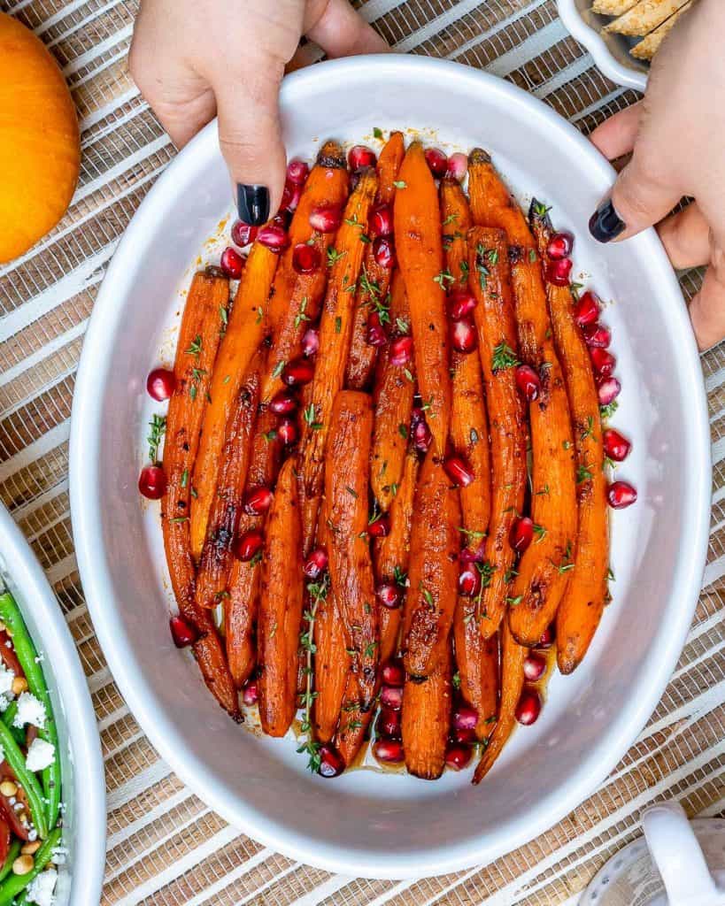 Roasted Carrots in a white dish with hand holding the dish