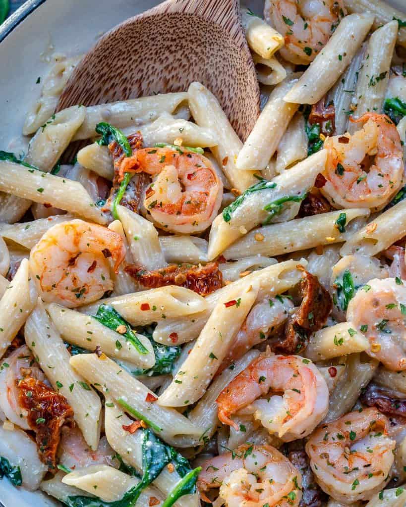 close up of shrimp and pasta with sundried tomatoes and spinach on a skillet