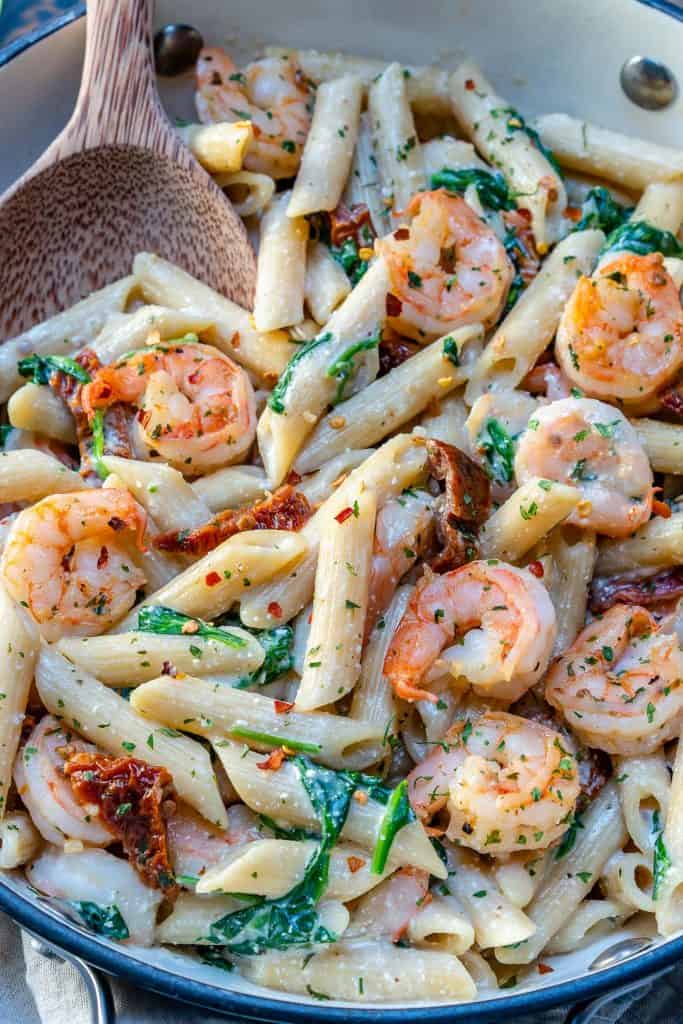 close up of creamy shrimp pasta in a pan with wooden spoon in skillet