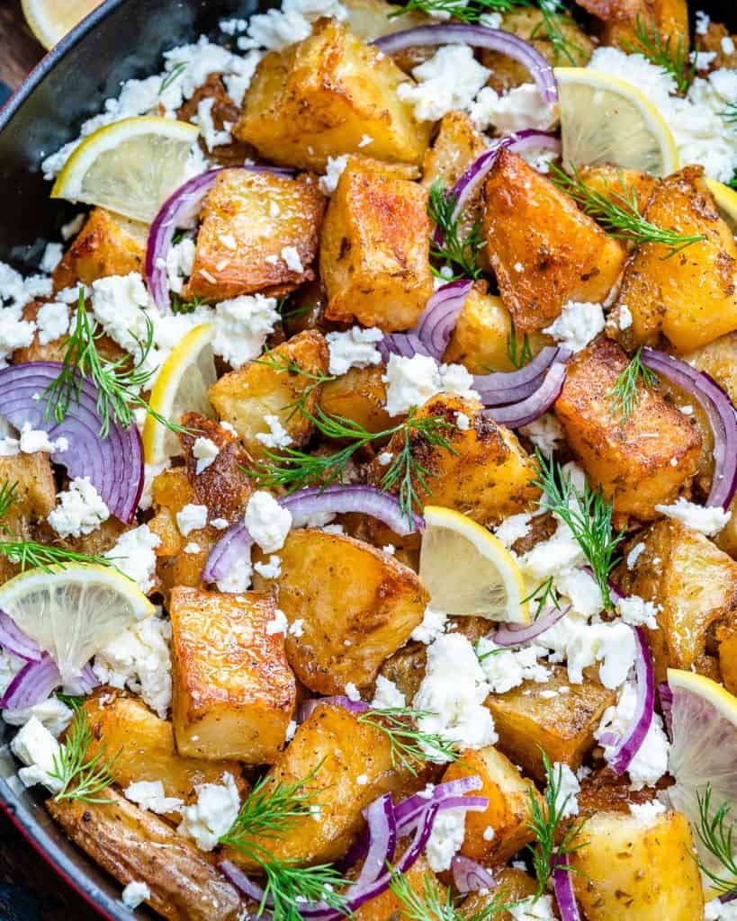 top-down shot of crispy looking potatoes topped with crumbled feta, sliced purple onions, sliced lemons, and chopped fill