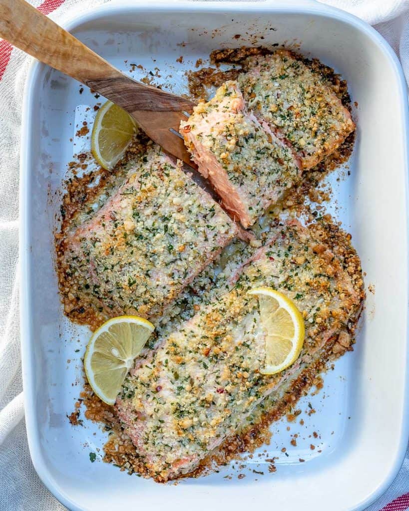 top view of 2 salmon filets with parmesan crust, topped with lemon slice, in a white dish