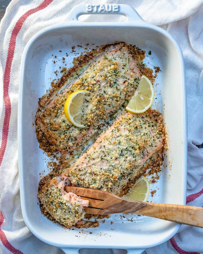 top view of 2 salmon filets with a crispy crust and wooden spoon into dish removing a morsel of salmon