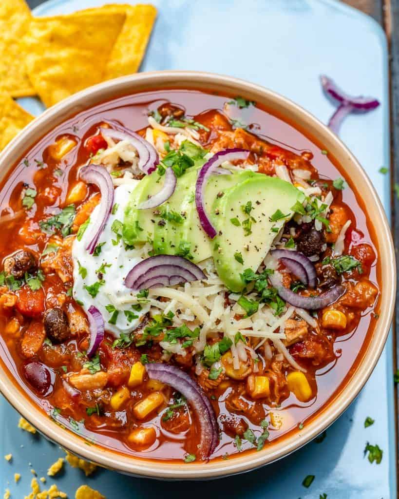 top view of a bowl of chili topped with sliced avocado and sour cream