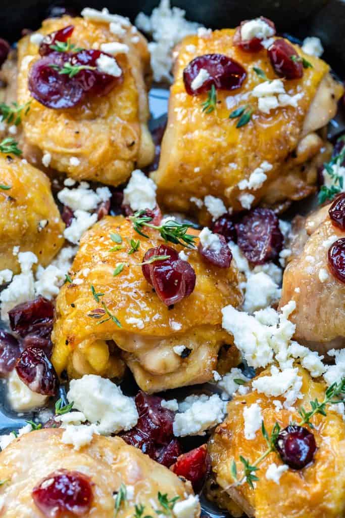 close up chicken thighs in a skillet topped with cranberries and feta cheese 