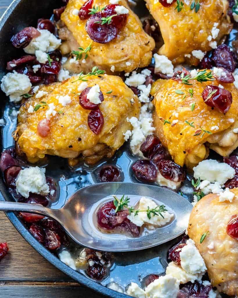 chicken thighs in skillet topped with cheese and cranberries