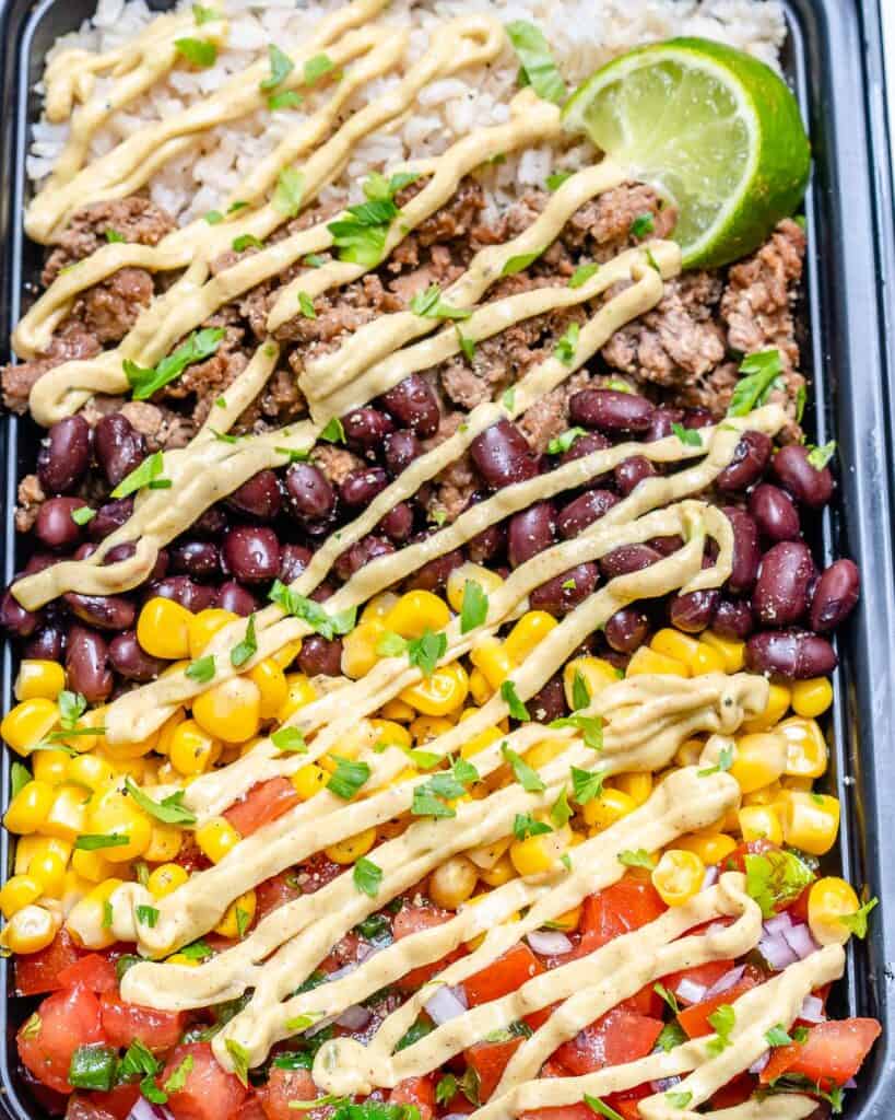 close up side shot of a beef burrito bowl with an avocado cream sauce drizzled over it