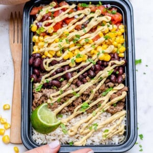 hand holding a black meal prep bowl with a beef burrito bowl with rice beans corn pico and ground beef.