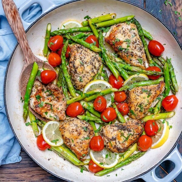 Seared chicken breast in a pan with asparagus and tomatoes.