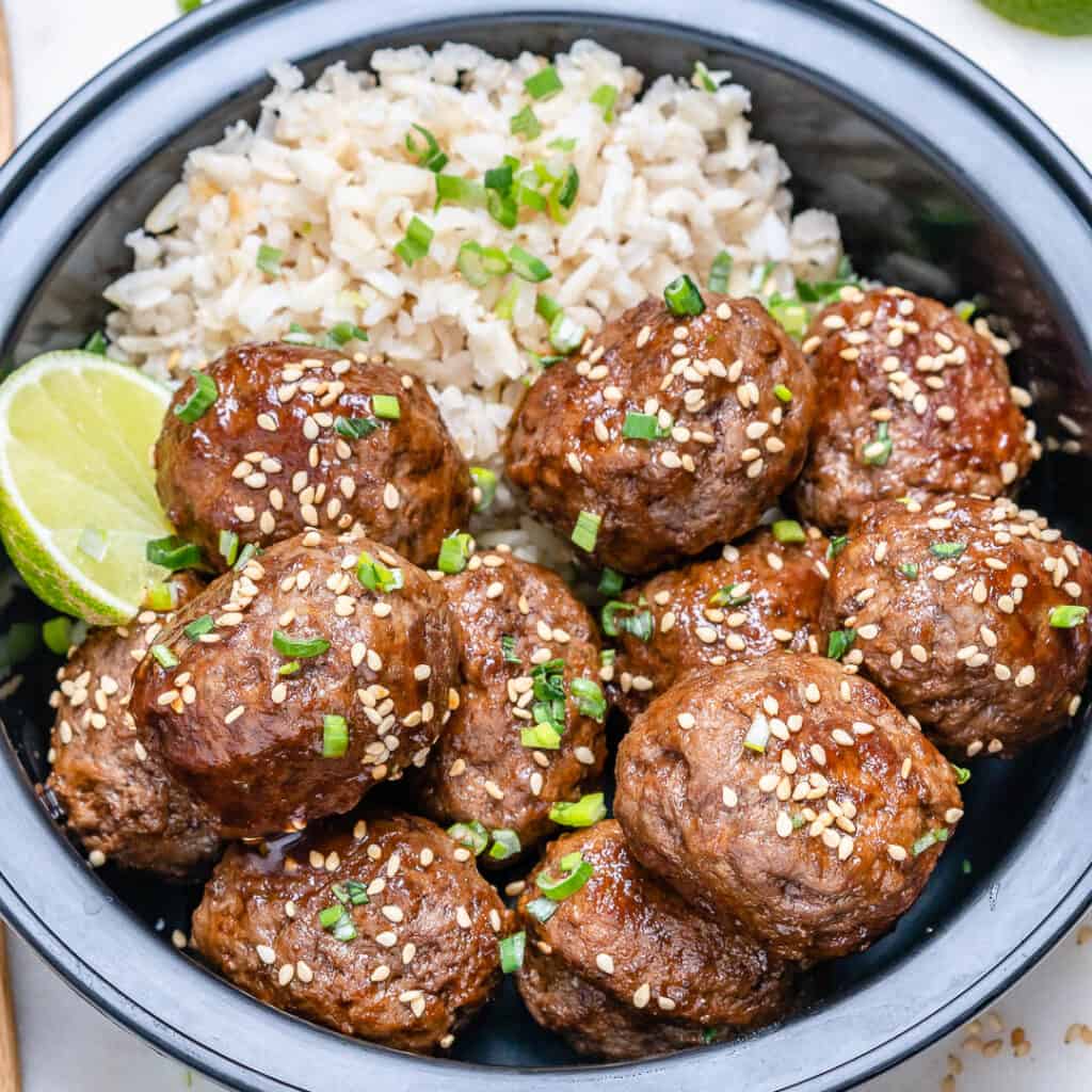side shot of meal prep meatballs with rice in a black bowl