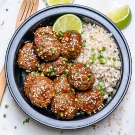 top view Asian meatballs with brown rice in a black meal prep bowl topped with sesame seeds