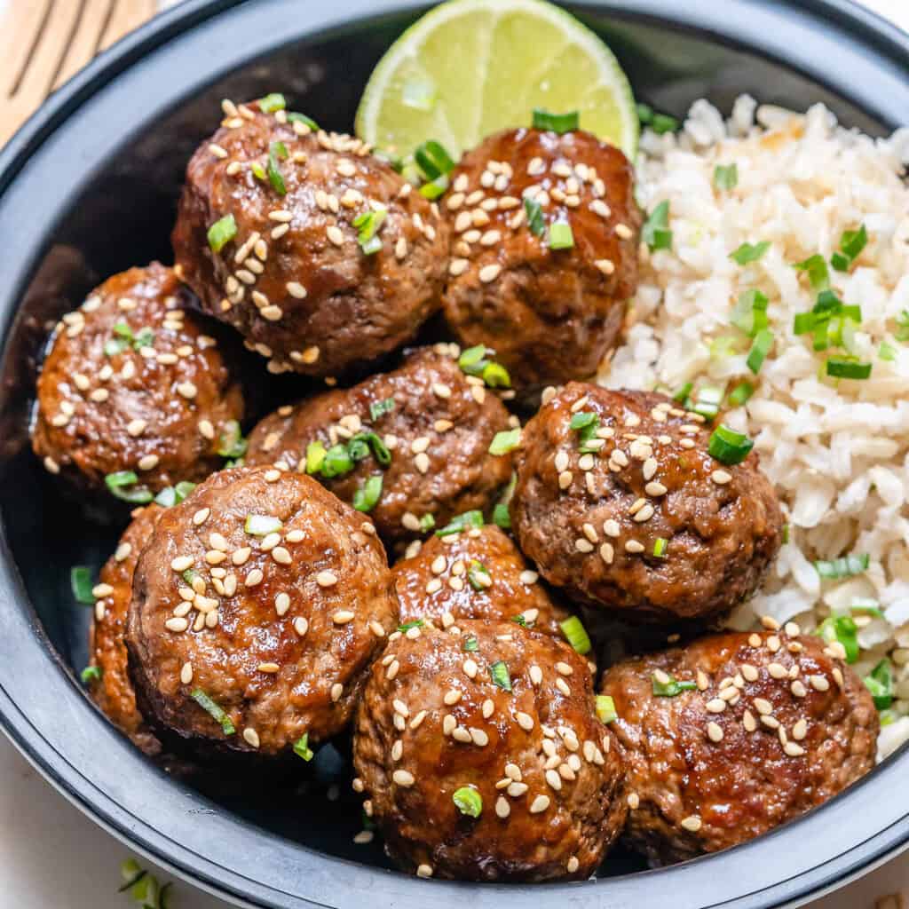 side shot of meatballs topped with sesame seeds with a side of rive in a bowl