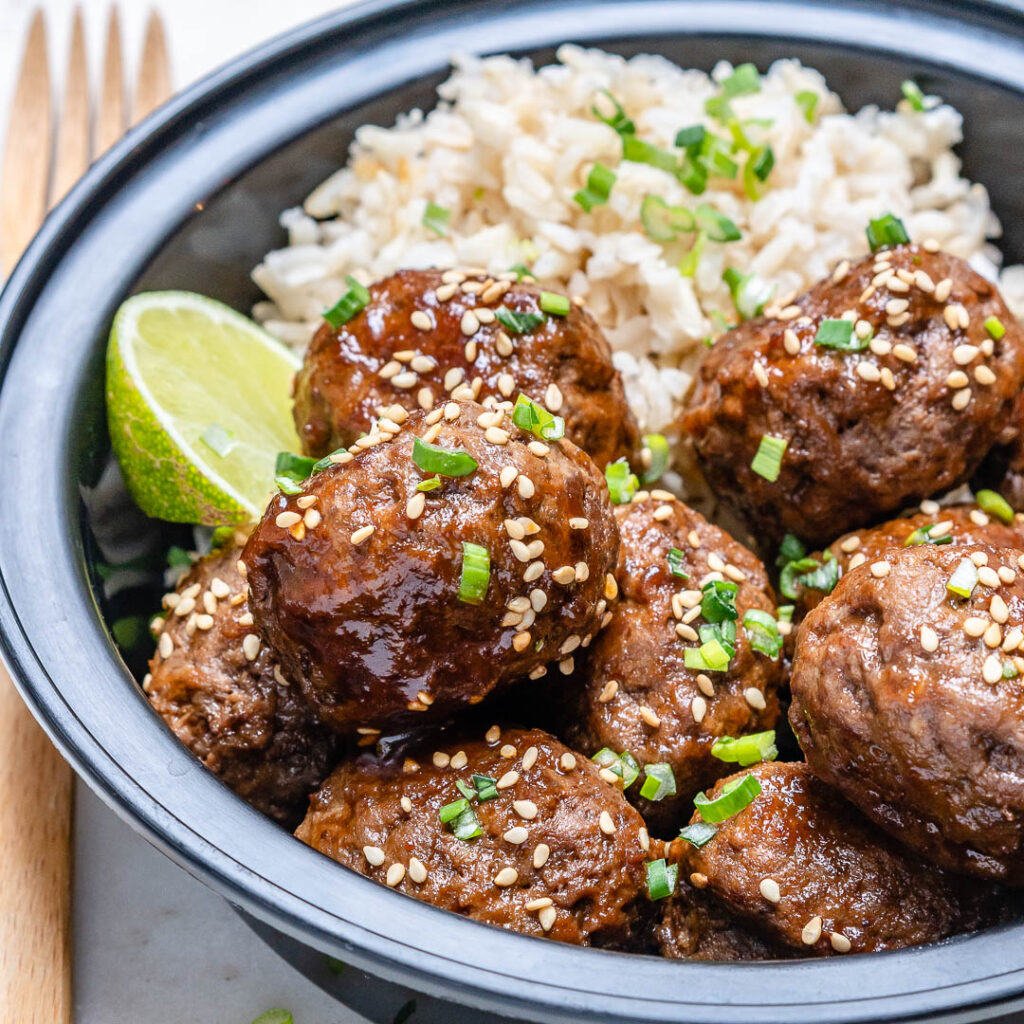 side shot of Asian meatballs in a black meal prep bowl with brown rice topped with sesame seeds