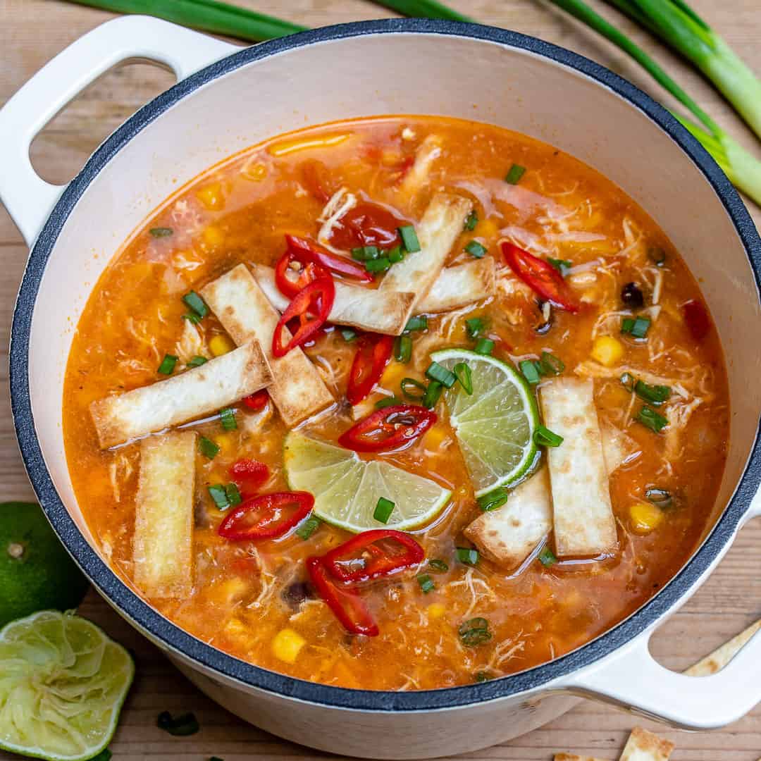 side view of a white dutch oven that has chicken tortilla soup topped with tortilla and sliced lime