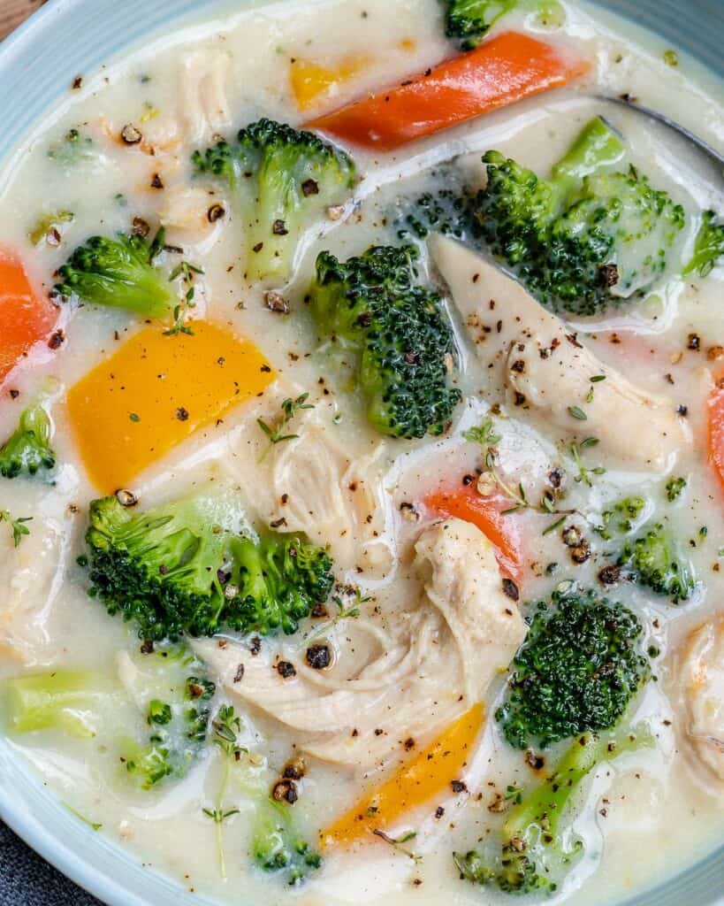 close up image of a bow if chicken soup that is creamy looking with broccoli and carrots