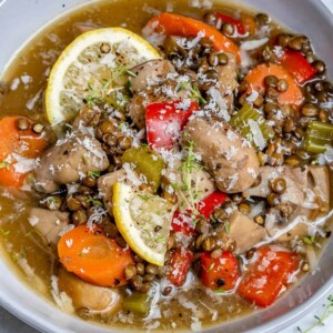 top view of a bowl of soup made of lentil, mushroom, and carrots, topped with lemon garnishes