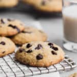 side shot of a single cookie on a wire rack next to 3 other cookies in the background with a cup of milk