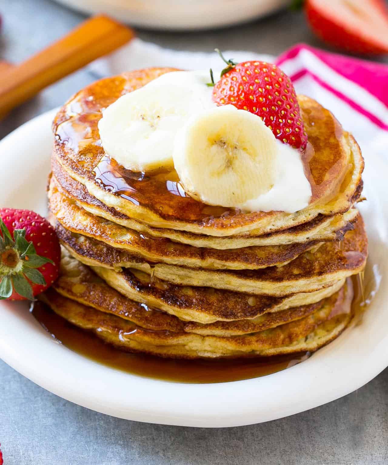 pancakes stacked on plate garnished with strawberries and syrup