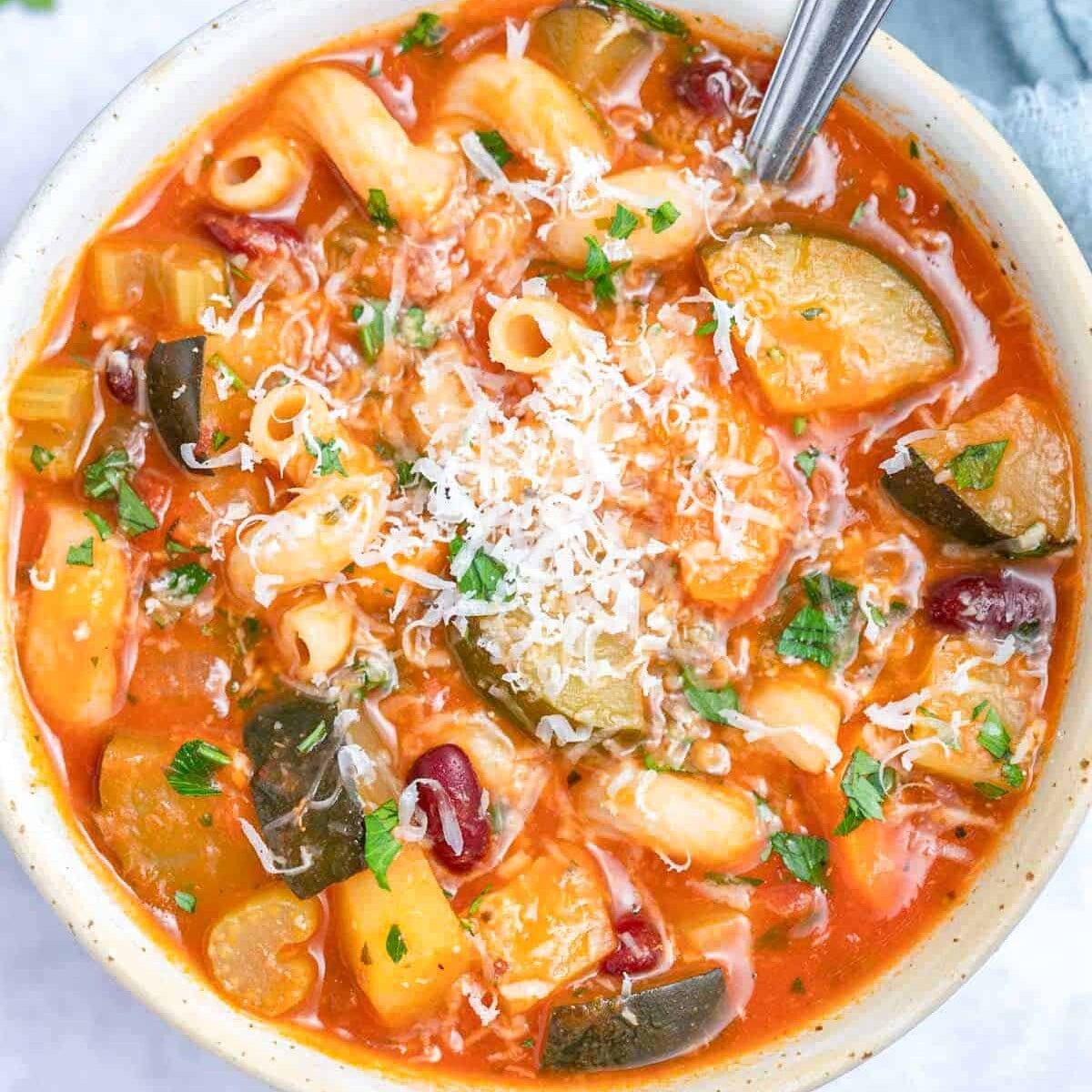 a round bowl with minestrone soup topped with parmesan cheese.