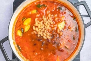 adding pasta and beans in a pot with sauce and veggies for soup.