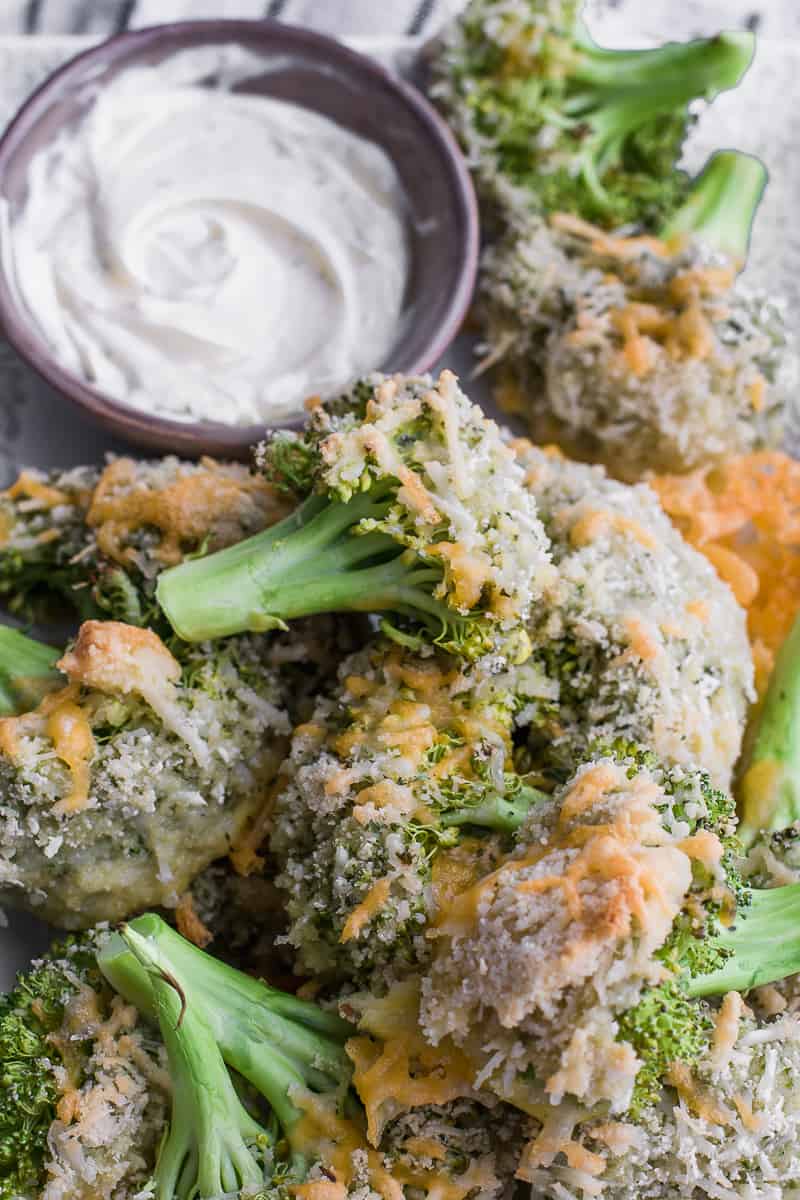 top view of a serving plate with baked broccoli on it and a small bowl of dipping white sauce 