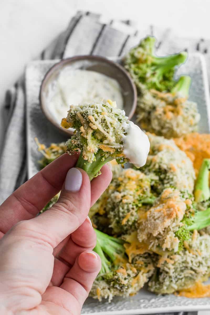 hand holding a single cheesy baked broccoli over the serving plate 